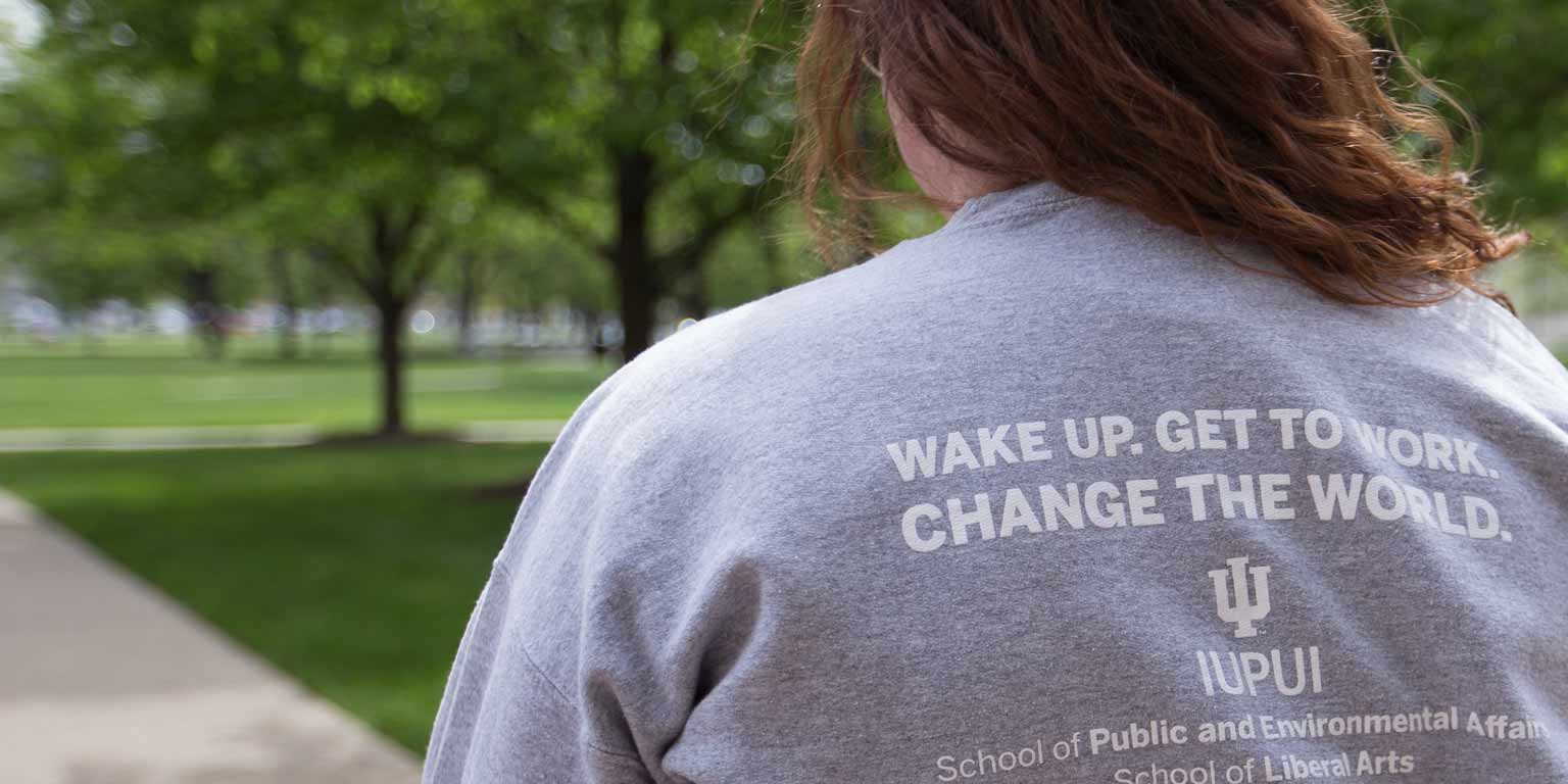 A student wears a SPEA shirt that says, 'Wake up. Get to work. Change the world.'